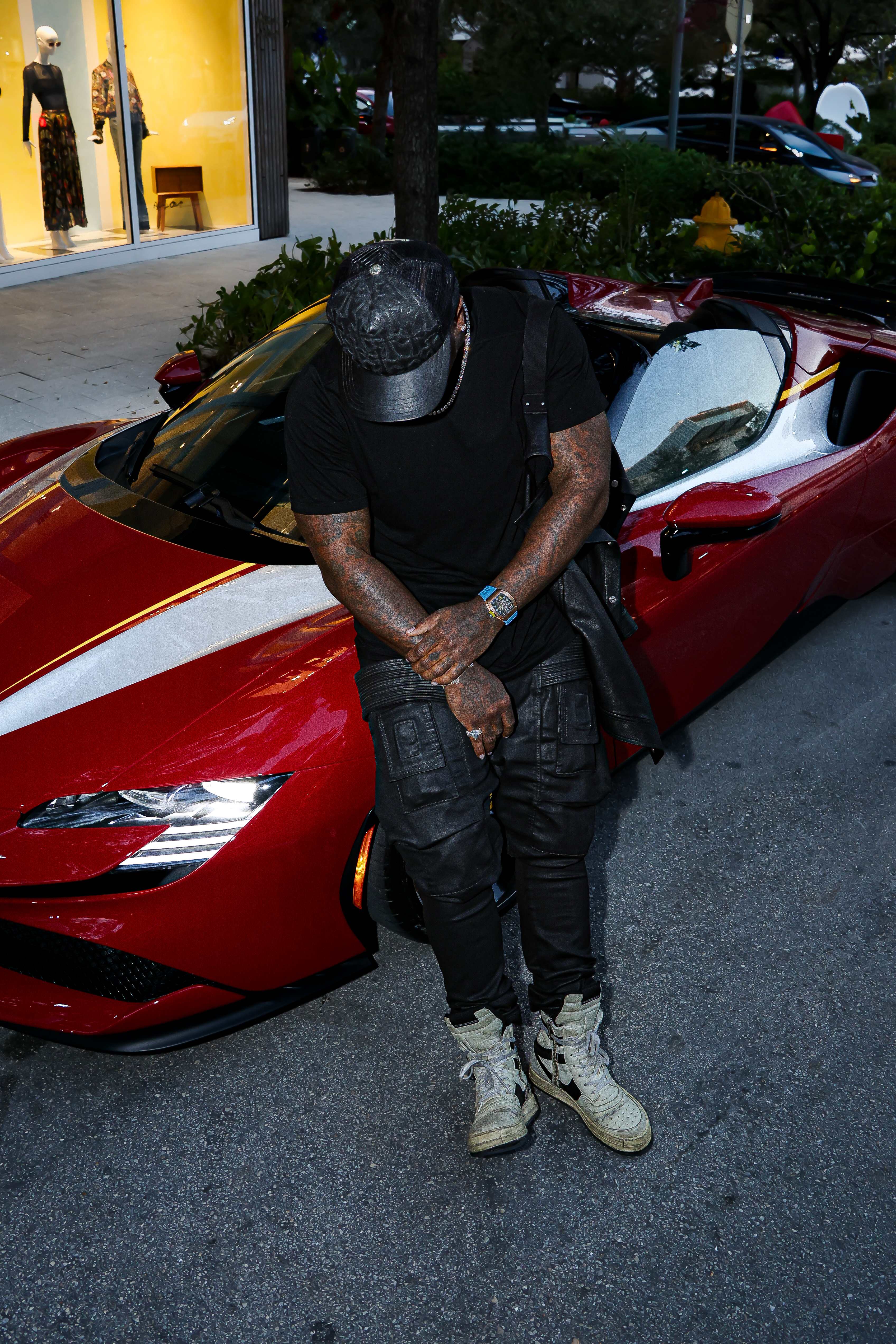 Man in all black leaning against a red Ferrari at dusk