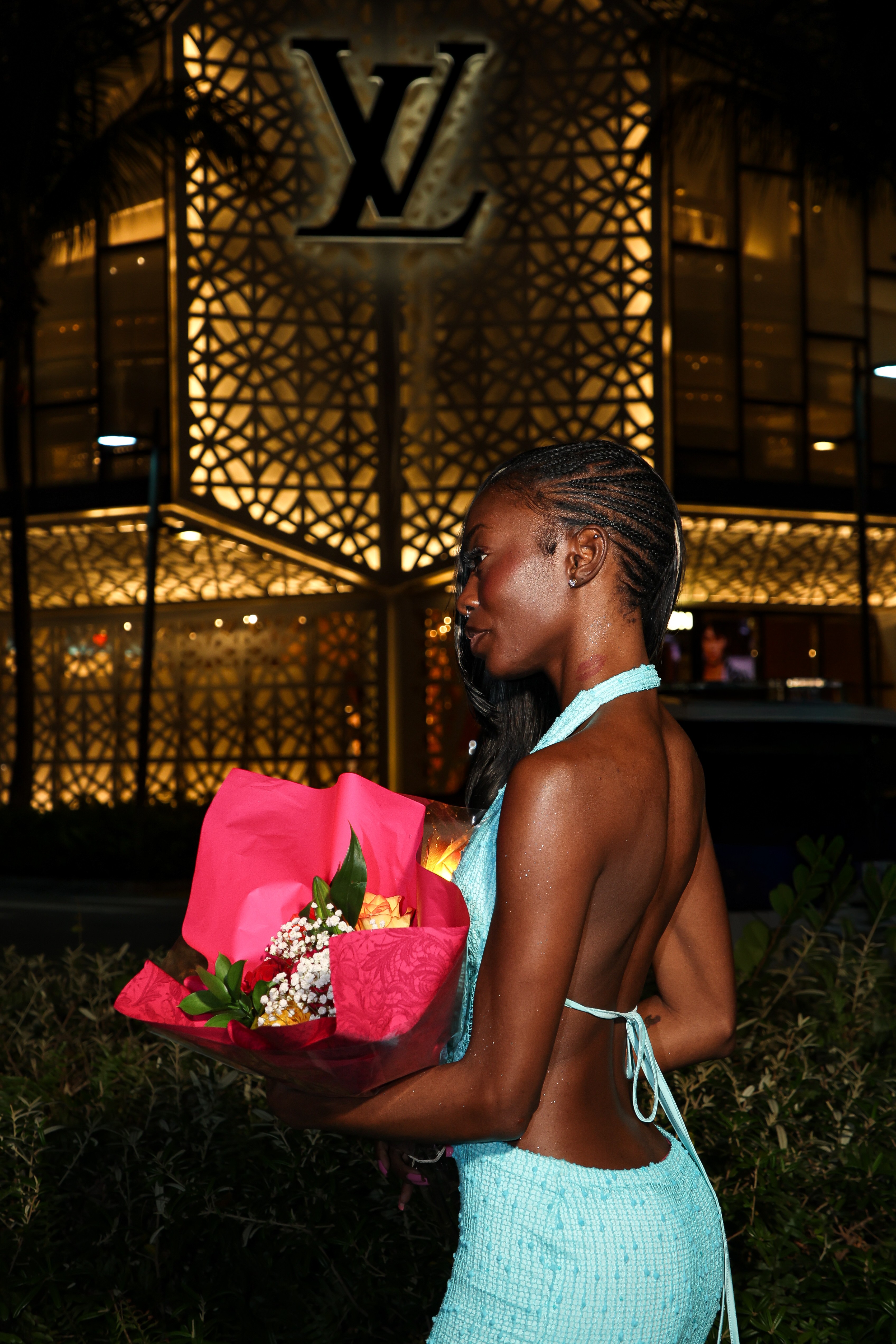 Woman in a backless dress in front of the illuminated Louis Vuitton facade at night
