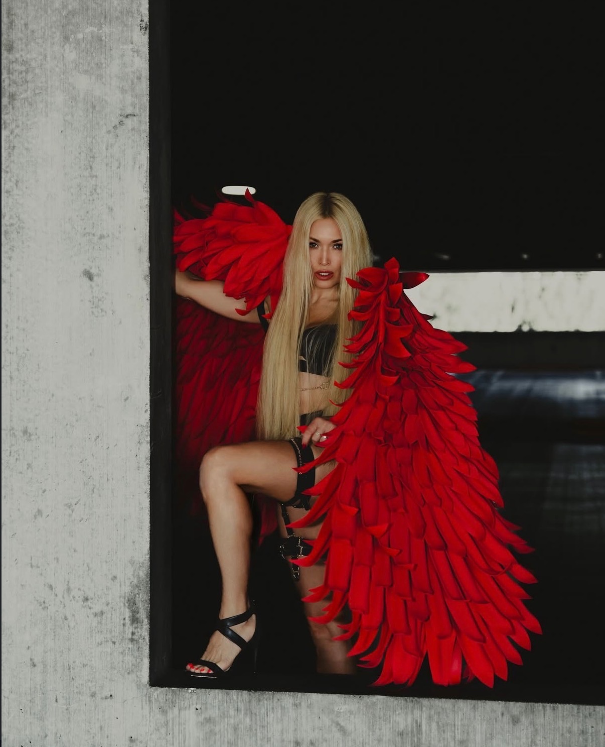 Styled editorial portrait with dramatic red feather wings